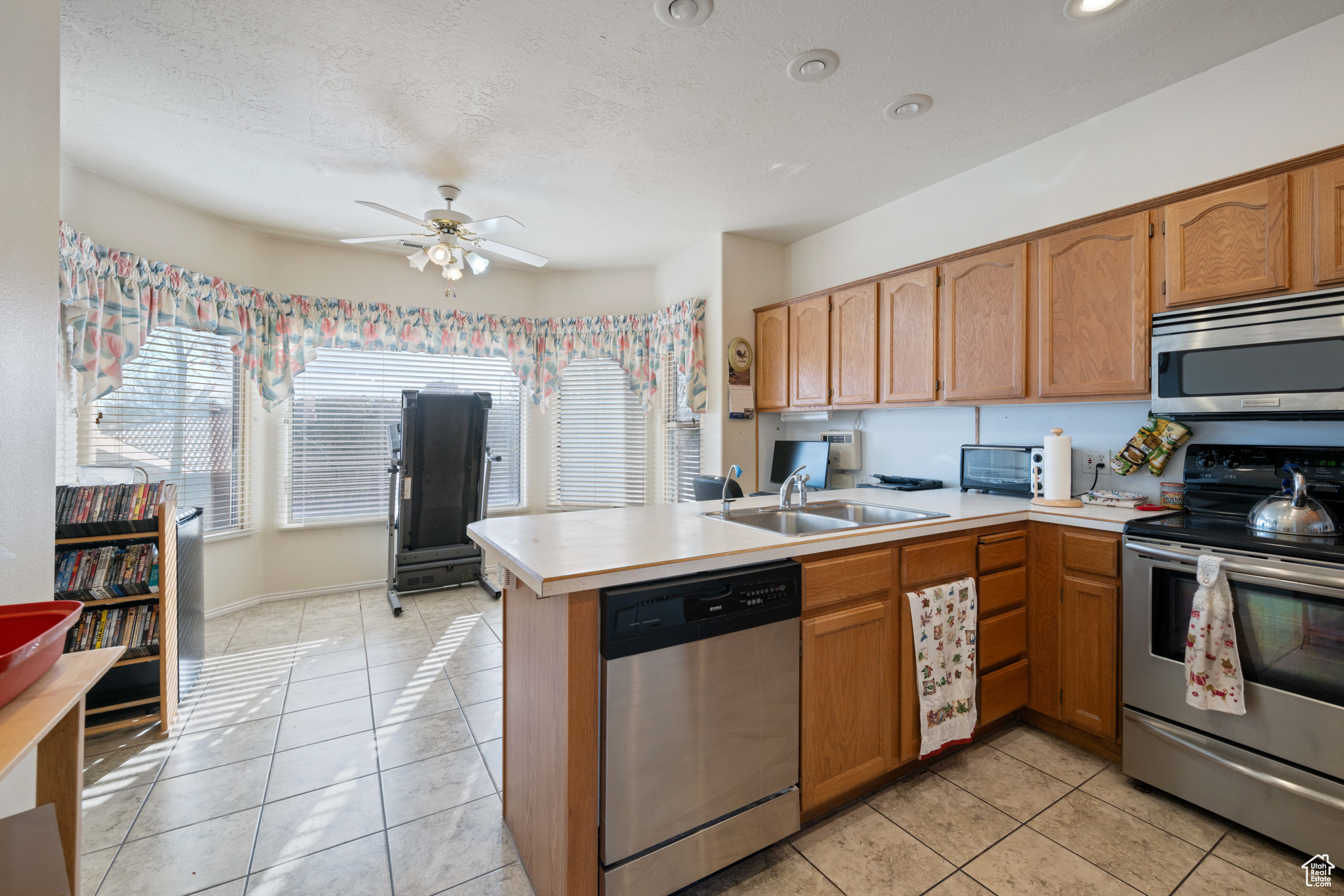 Kitchen with ceiling fan, sink, stainless steel appliances, kitchen peninsula, and light tile patterned floors