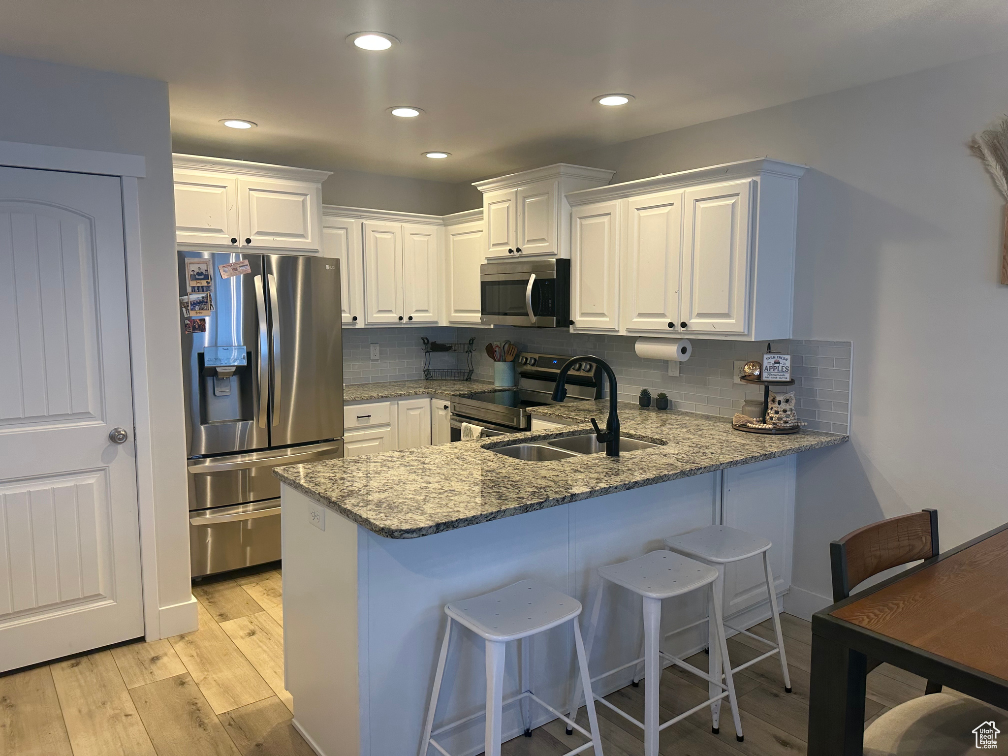 Kitchen with white cabinets, sink, light hardwood / wood-style flooring, appliances with stainless steel finishes, and stone countertops