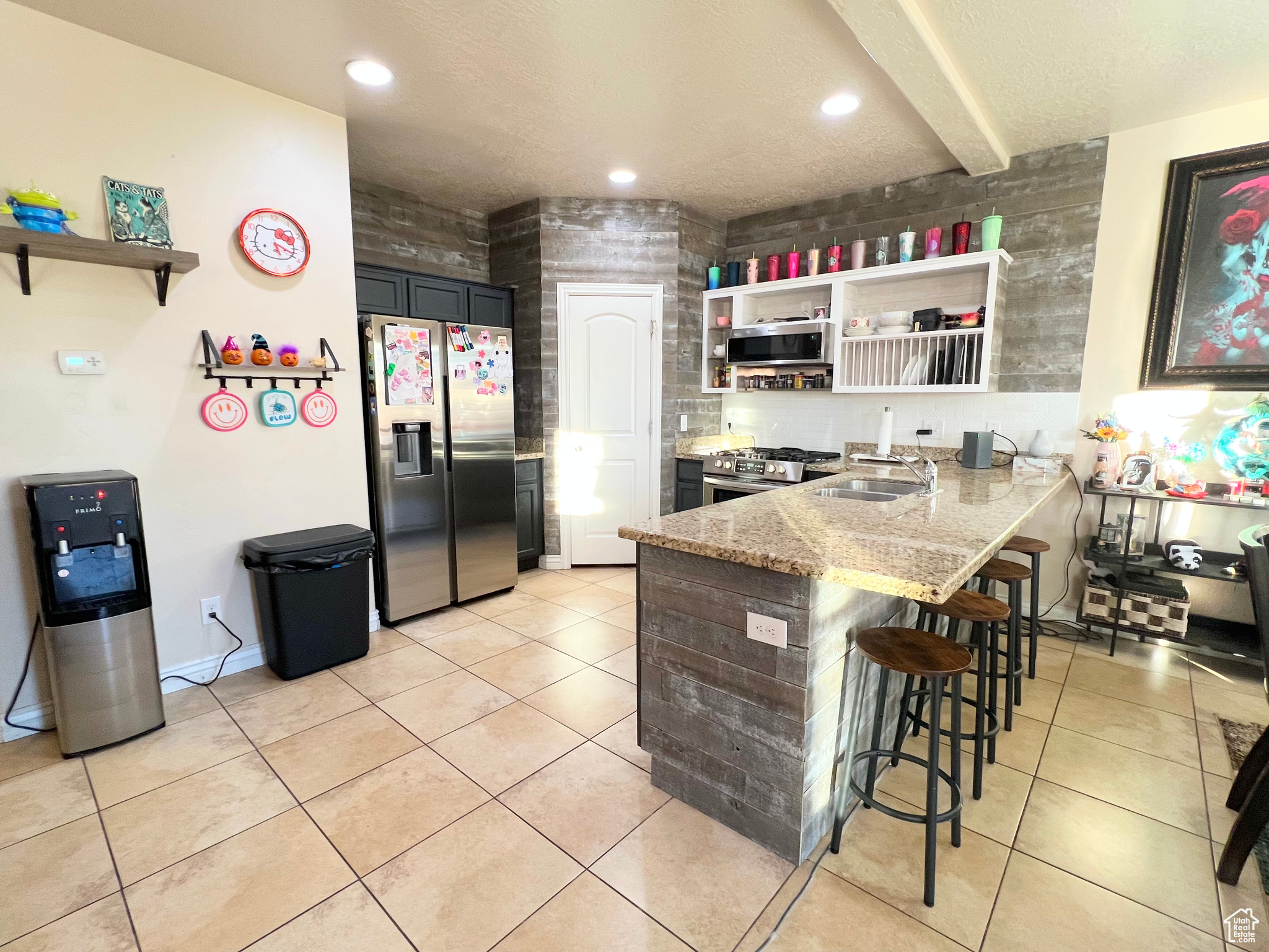 Kitchen with kitchen peninsula, light stone counters, a breakfast bar, stainless steel appliances, and sink