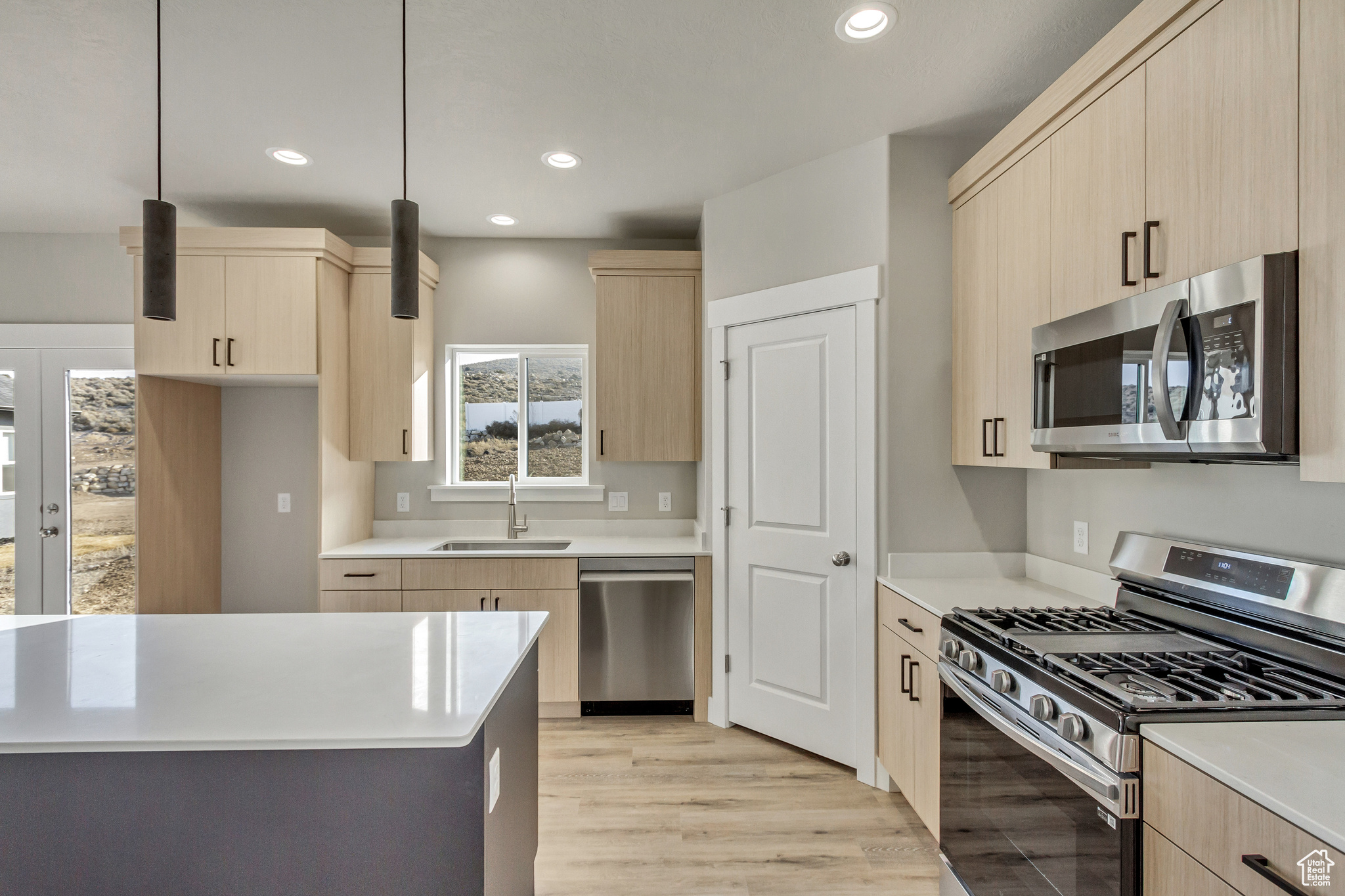 Kitchen with appliances with stainless steel finishes, light brown cabinets, pendant lighting, and sink