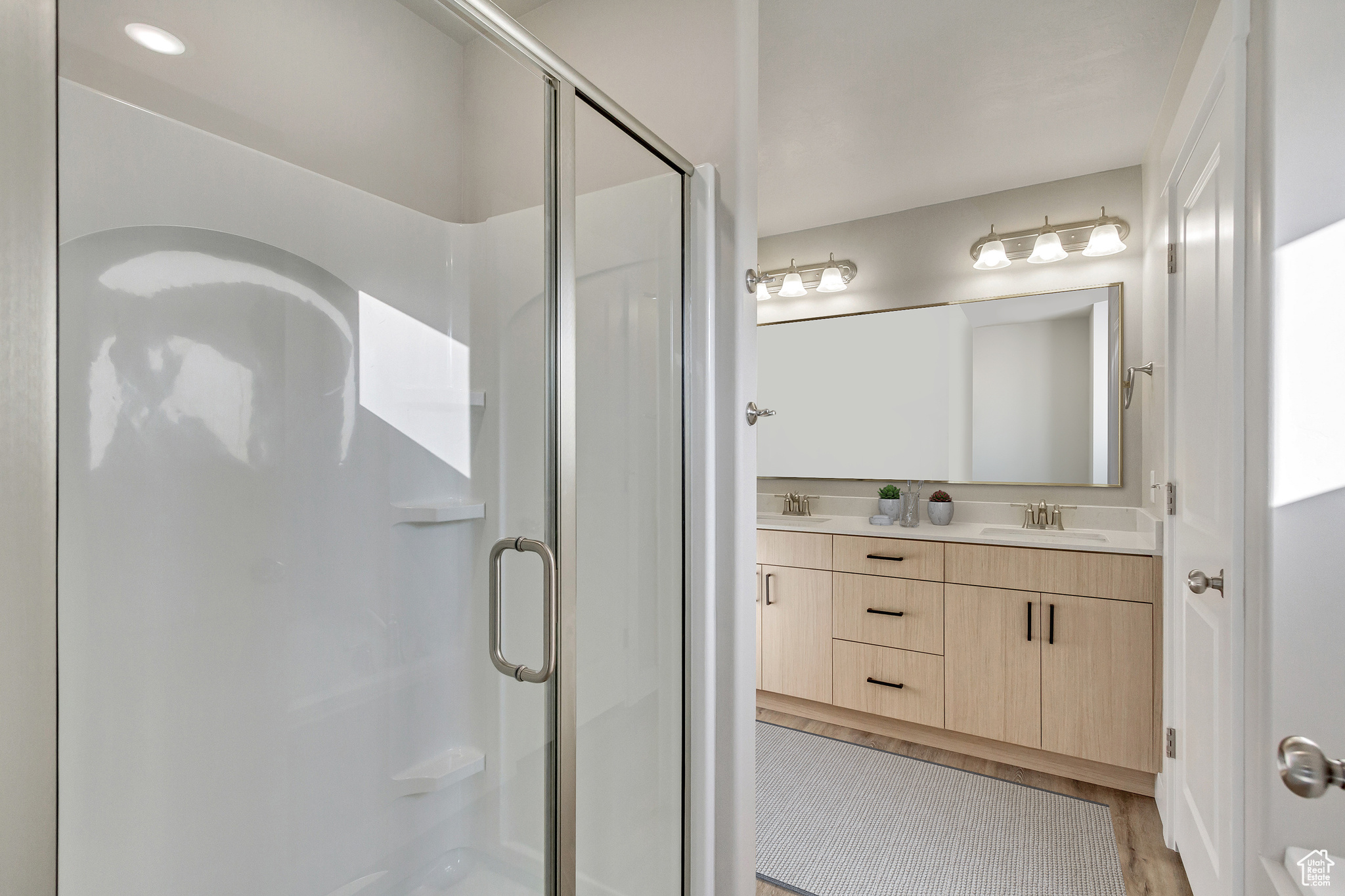 Bathroom with vanity, a shower with shower door, and wood-type flooring