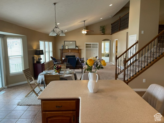 Kitchen featuring pendant lighting, lofted ceiling, ceiling fan with notable chandelier, a fireplace, and light tile patterned flooring