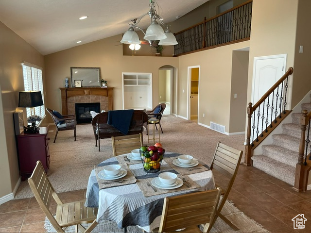 Tiled dining space featuring a tile fireplace, high vaulted ceiling, and a chandelier