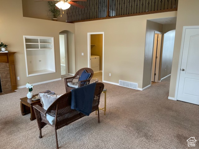 Sitting room with light carpet, a high ceiling, built in shelves, ceiling fan, and washer / clothes dryer