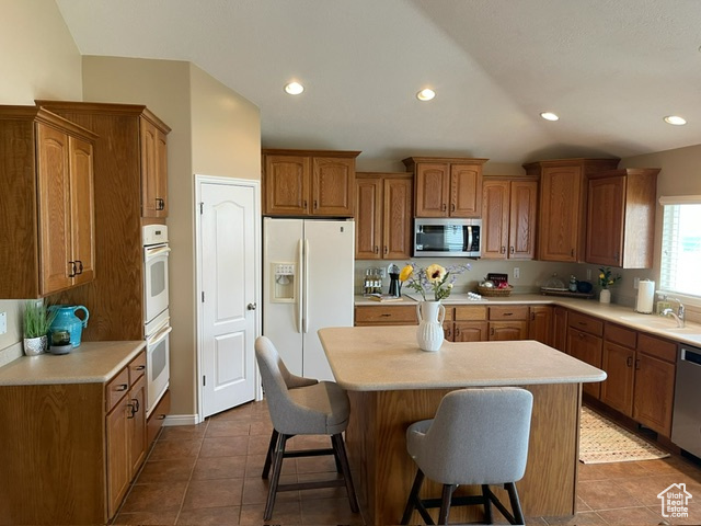 Kitchen featuring stainless steel appliances, sink, tile patterned flooring, a kitchen island, and a breakfast bar area