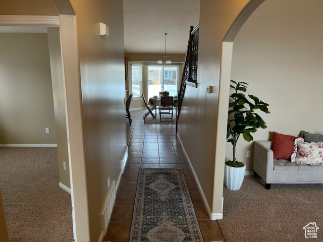 Hall featuring dark carpet and an inviting chandelier