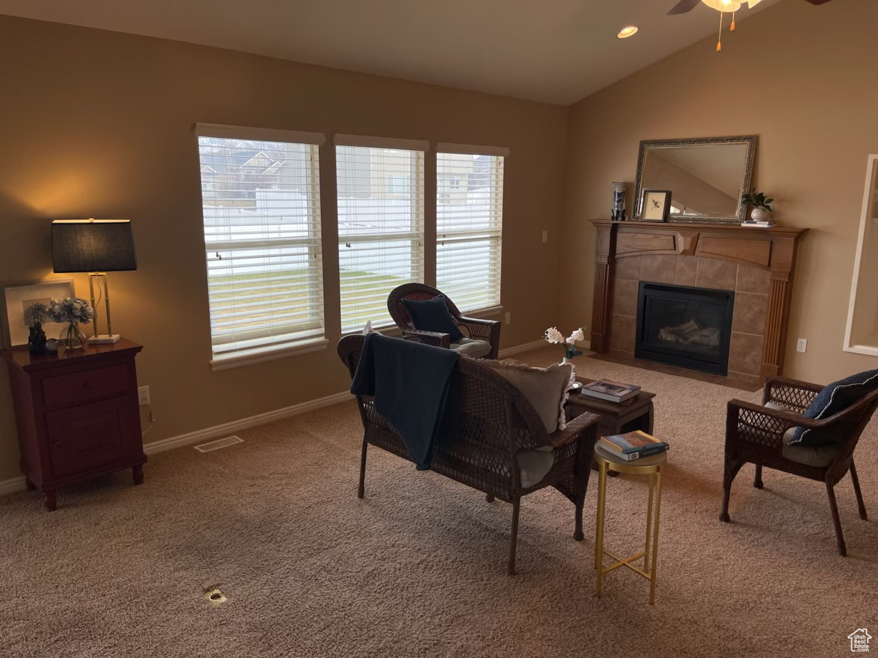 Carpeted living room with a tiled fireplace, ceiling fan, and vaulted ceiling