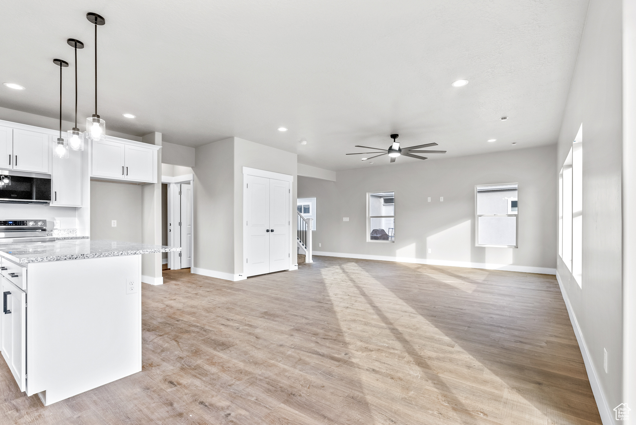 Kitchen with ceiling fan, stainless steel appliances, light stone counters, light hardwood / wood-style floors, and white cabinets