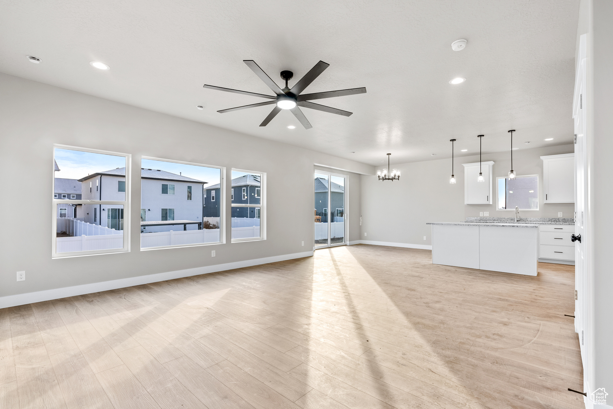 Unfurnished living room featuring ceiling fan with notable chandelier and light wood-type flooring