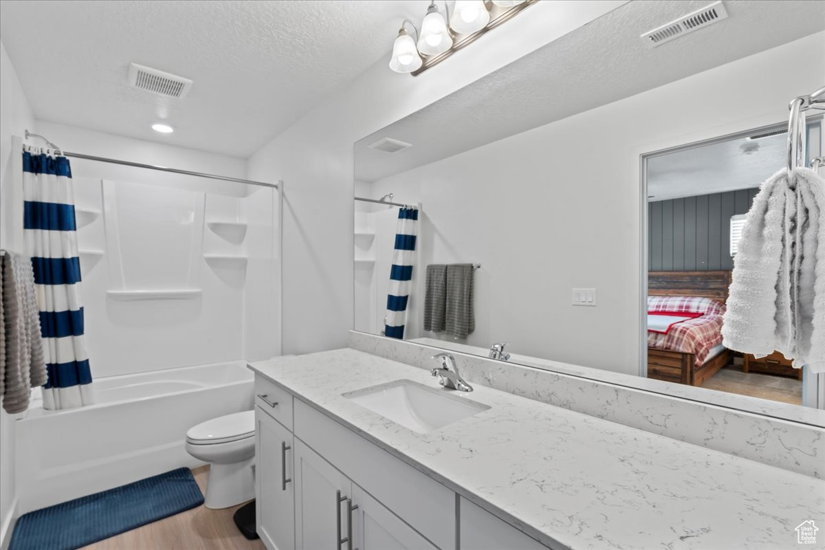 Full bathroom featuring wood-type flooring, a textured ceiling, toilet, shower / tub combo with curtain, and vanity