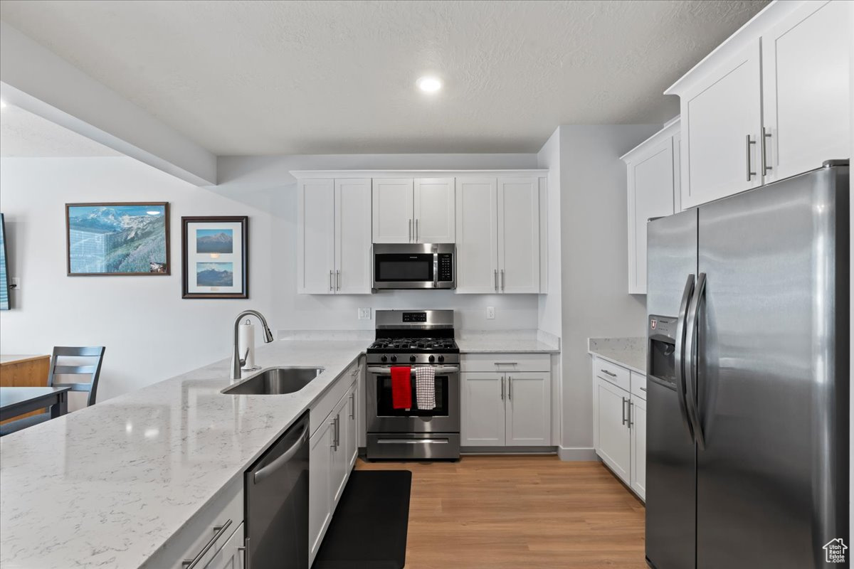 Kitchen with white cabinets, sink, light wood-type flooring, light stone countertops, and appliances with stainless steel finishes