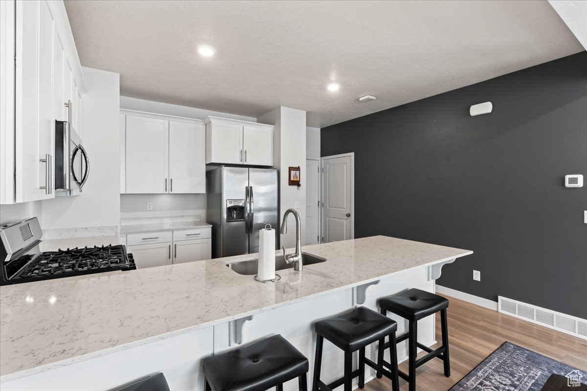 Kitchen featuring sink, light stone countertops, appliances with stainless steel finishes, a kitchen bar, and white cabinetry