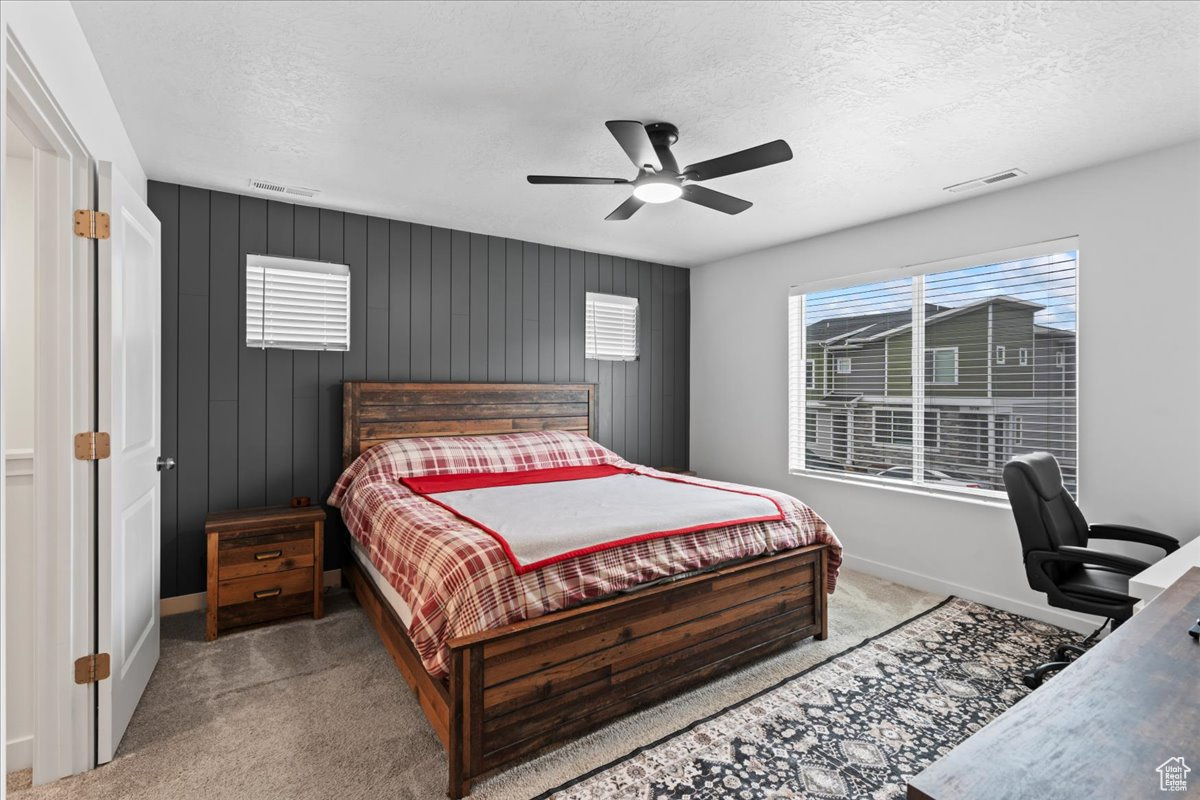 Carpeted bedroom featuring a textured ceiling, ceiling fan, and wood walls