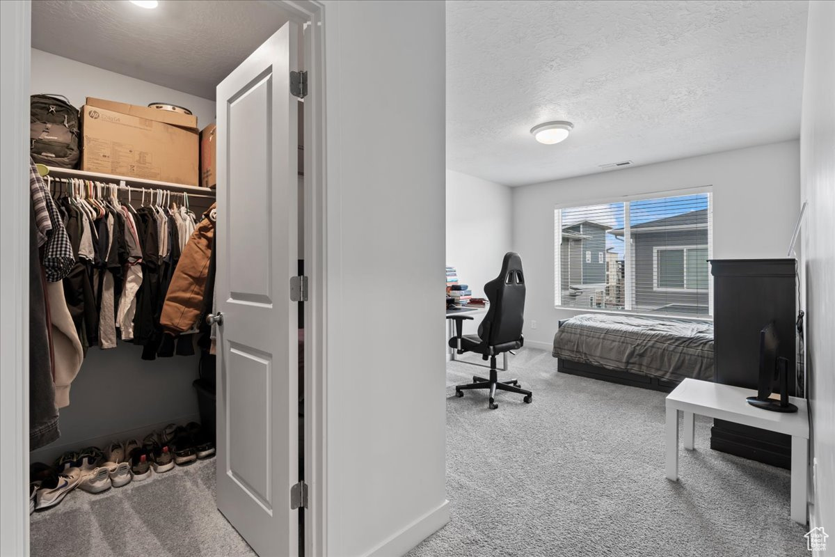 Carpeted bedroom with a spacious closet, a textured ceiling, and a closet