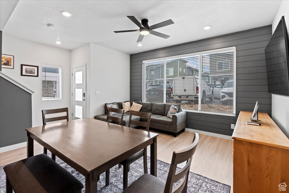 Dining space featuring a textured ceiling, light hardwood / wood-style floors, ceiling fan, and wooden walls