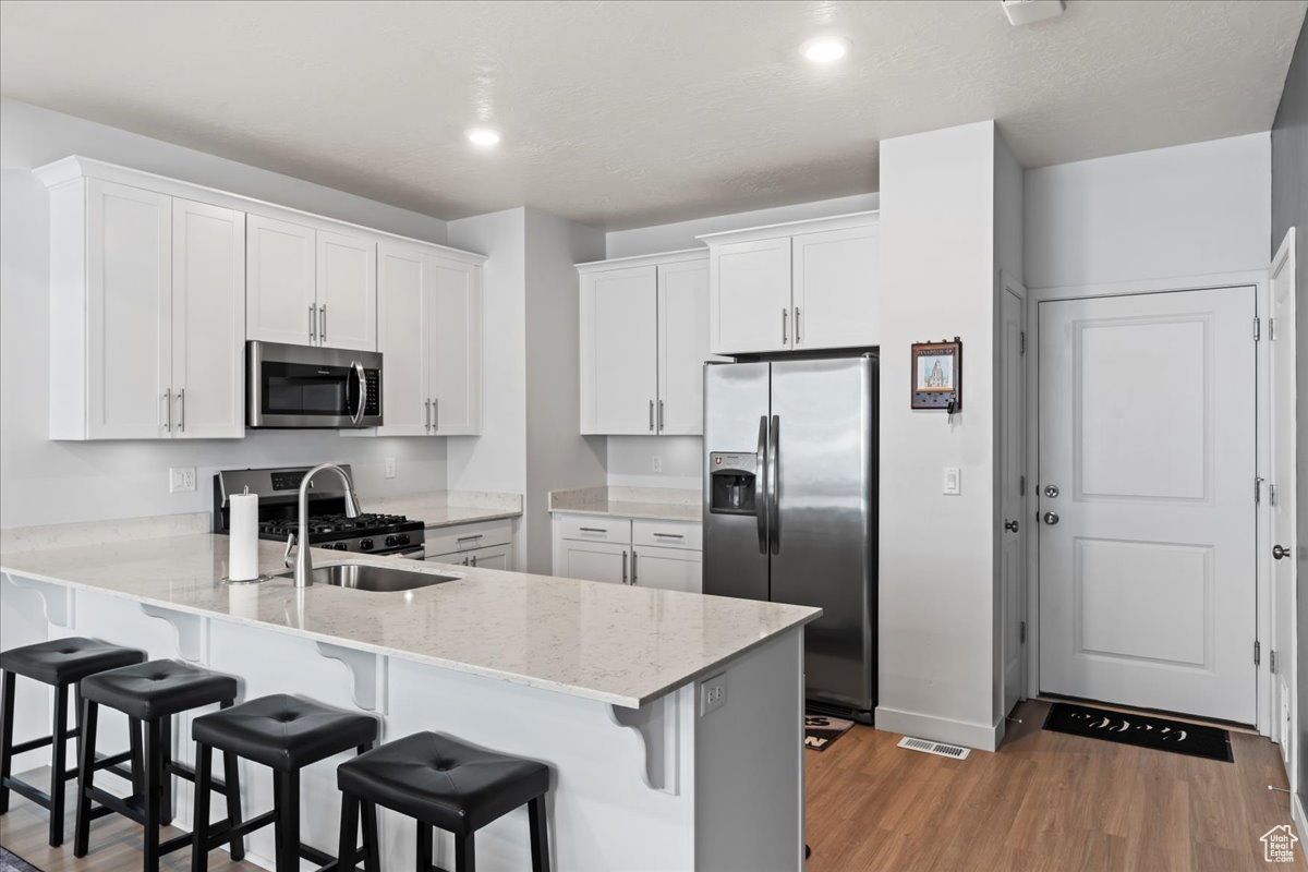 Kitchen featuring kitchen peninsula, a kitchen bar, stainless steel appliances, light hardwood / wood-style flooring, and white cabinetry