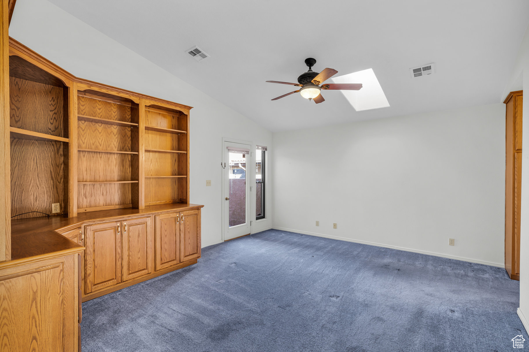 Unfurnished living room with dark colored carpet, ceiling fan, and vaulted ceiling with skylight