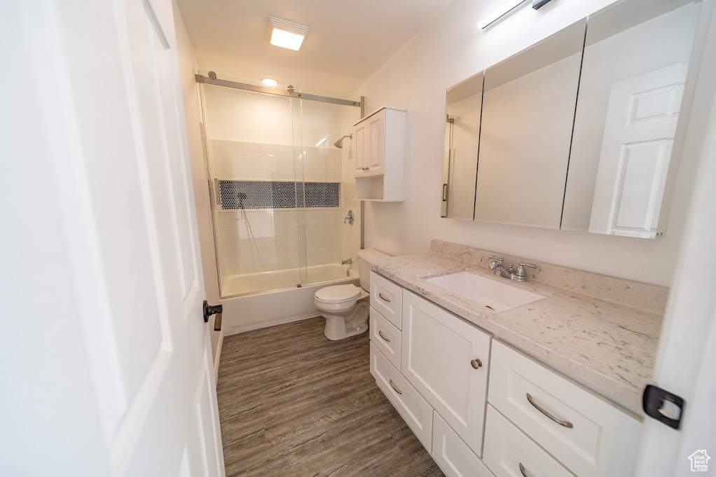 Full bathroom featuring vanity, toilet, combined bath / shower with glass door, and wood-type flooring