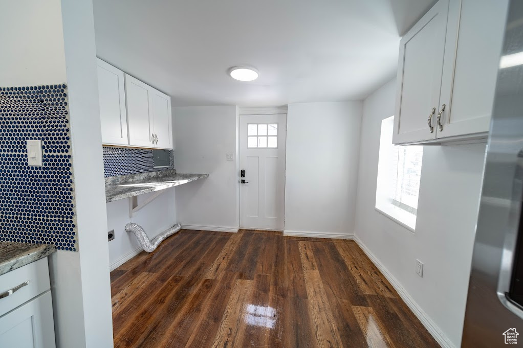 Kitchen with dark wood-type flooring, white cabinets, tasteful backsplash, stone countertops, and stainless steel refrigerator