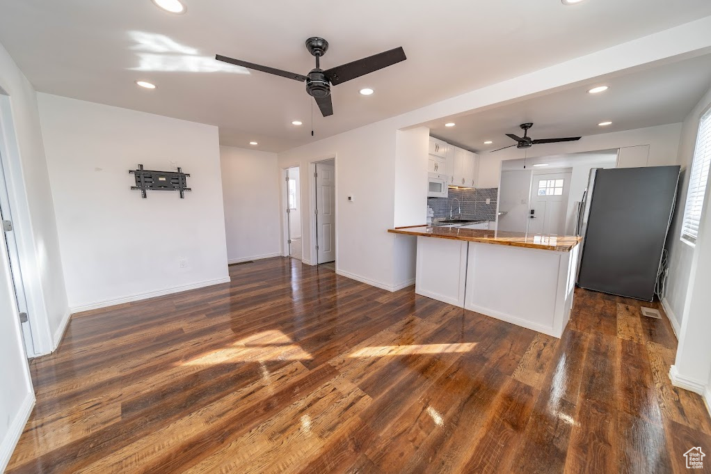 Kitchen featuring stainless steel fridge, tasteful backsplash, white cabinetry, dark hardwood / wood-style flooring, and kitchen peninsula