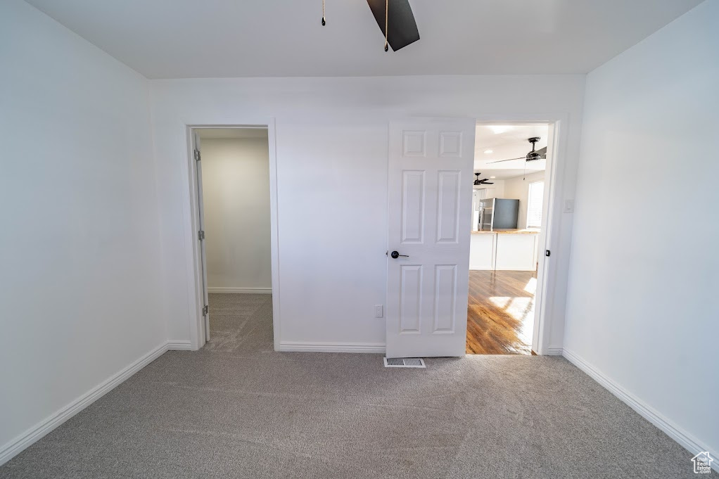 Unfurnished bedroom featuring carpet, stainless steel fridge, a spacious closet, and ceiling fan