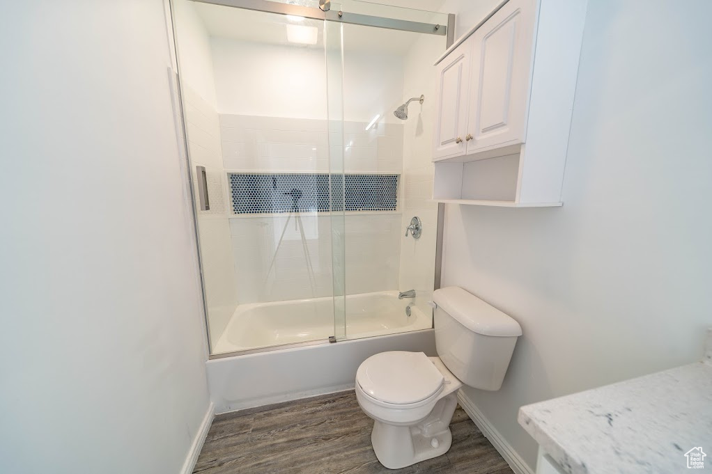 Bathroom featuring toilet, bath / shower combo with glass door, and hardwood / wood-style flooring