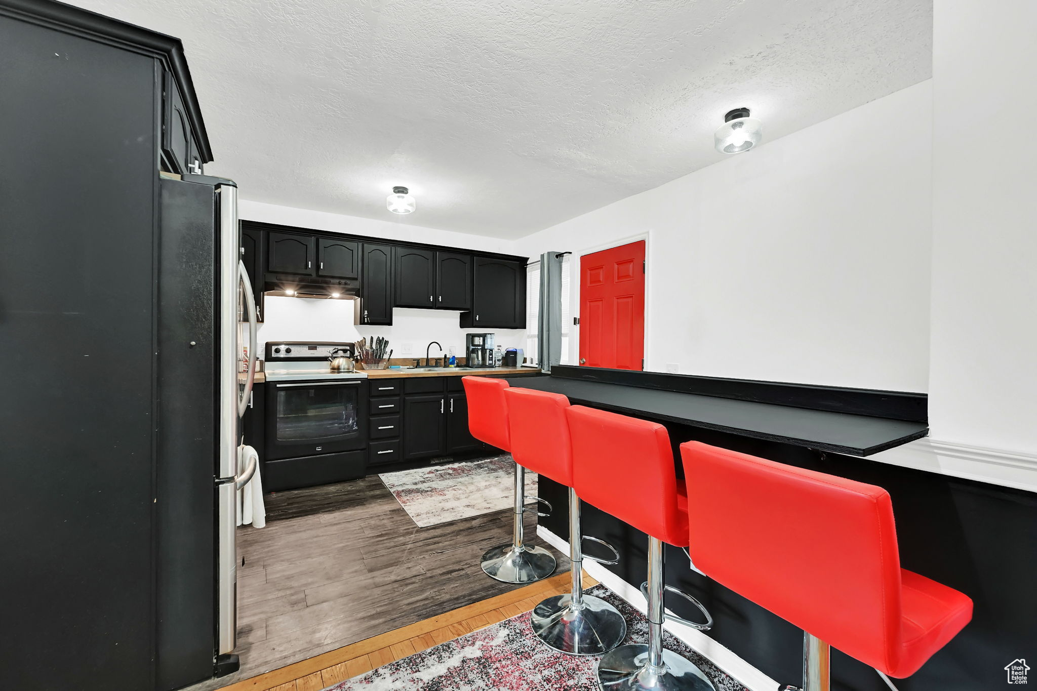 Kitchen with a textured ceiling, dark hardwood / wood-style floors, range with electric stovetop, and sink