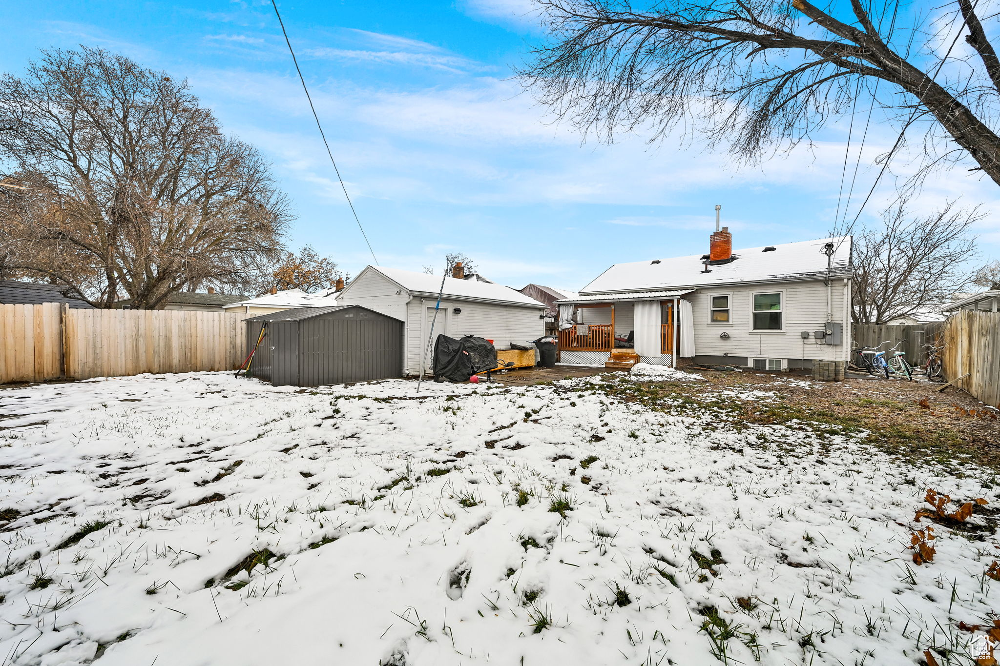 Snow covered back of property with an outbuilding and a wooden deck