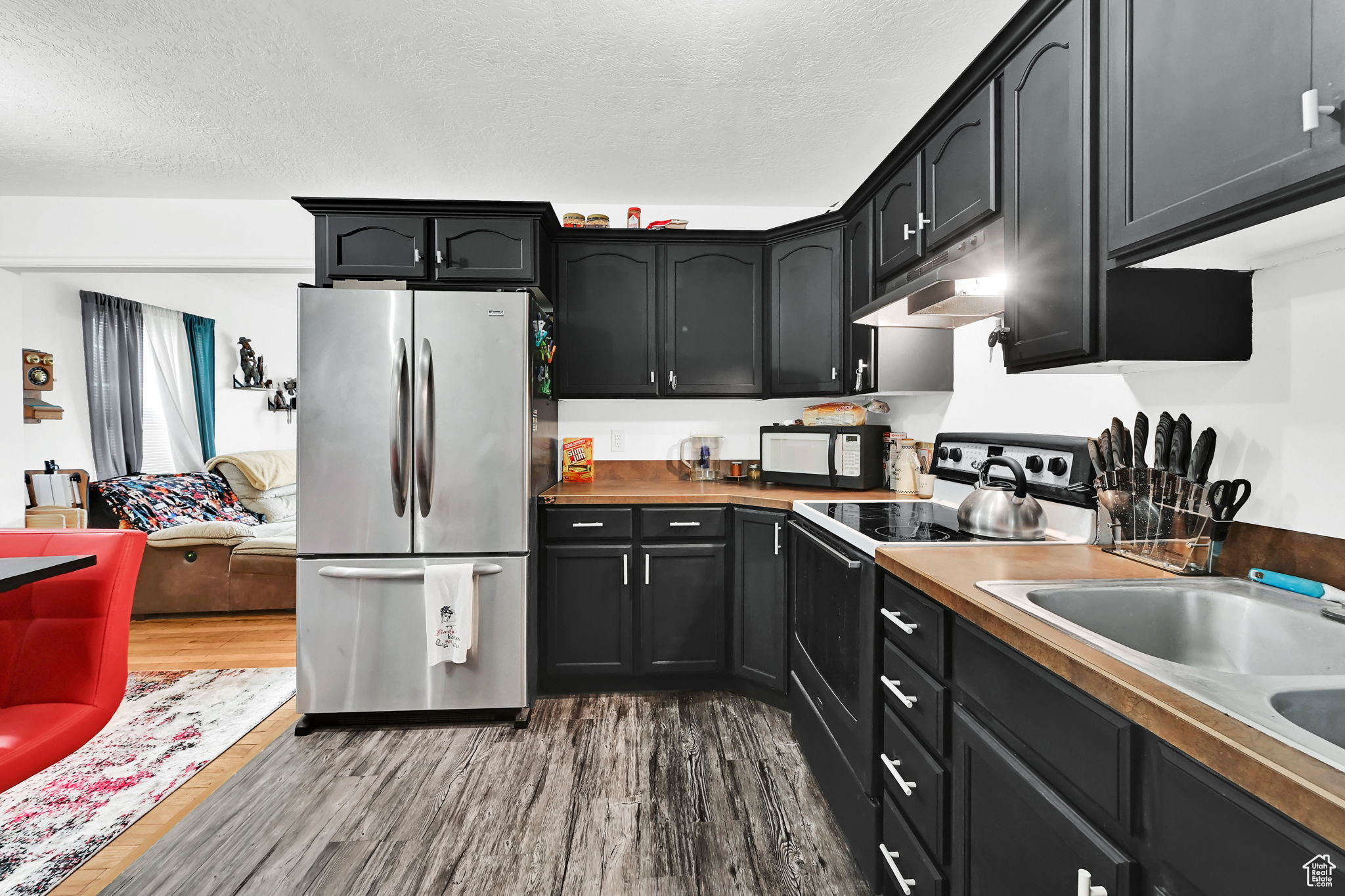 Kitchen with stainless steel refrigerator, sink, a textured ceiling, electric stove, and hardwood / wood-style flooring