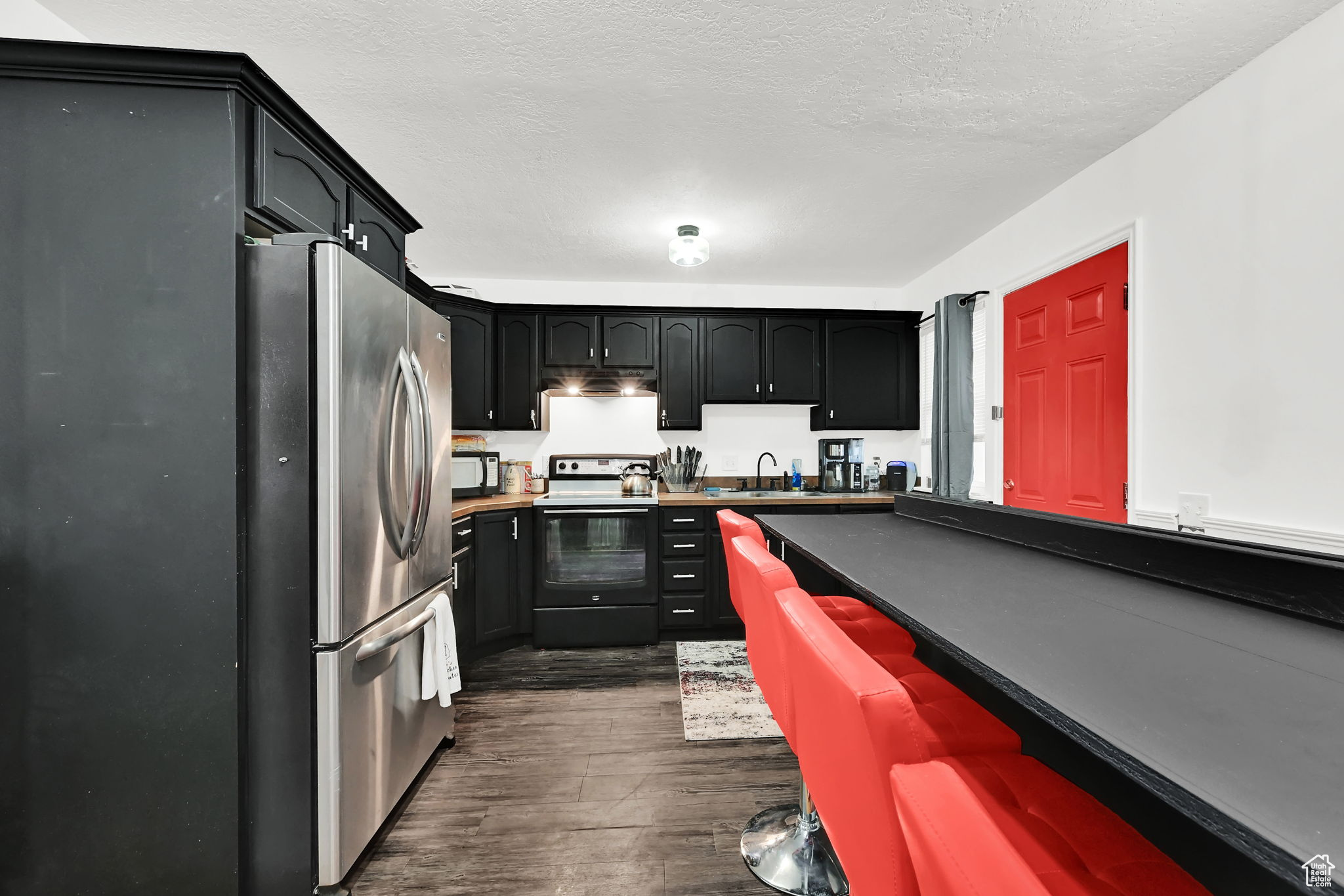 Kitchen with stainless steel fridge, dark hardwood / wood-style flooring, a textured ceiling, sink, and electric stove