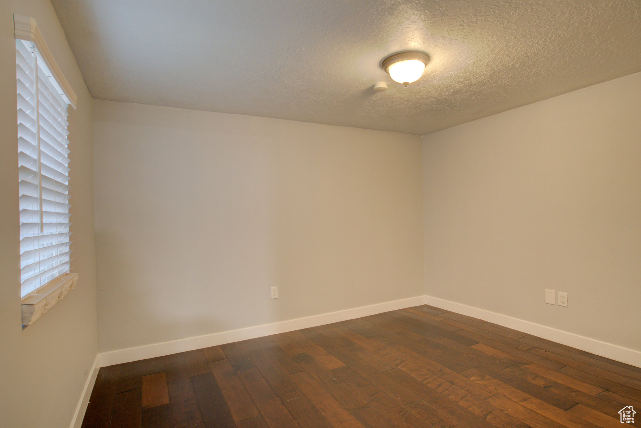 Empty room with a textured ceiling and dark wood-type flooring