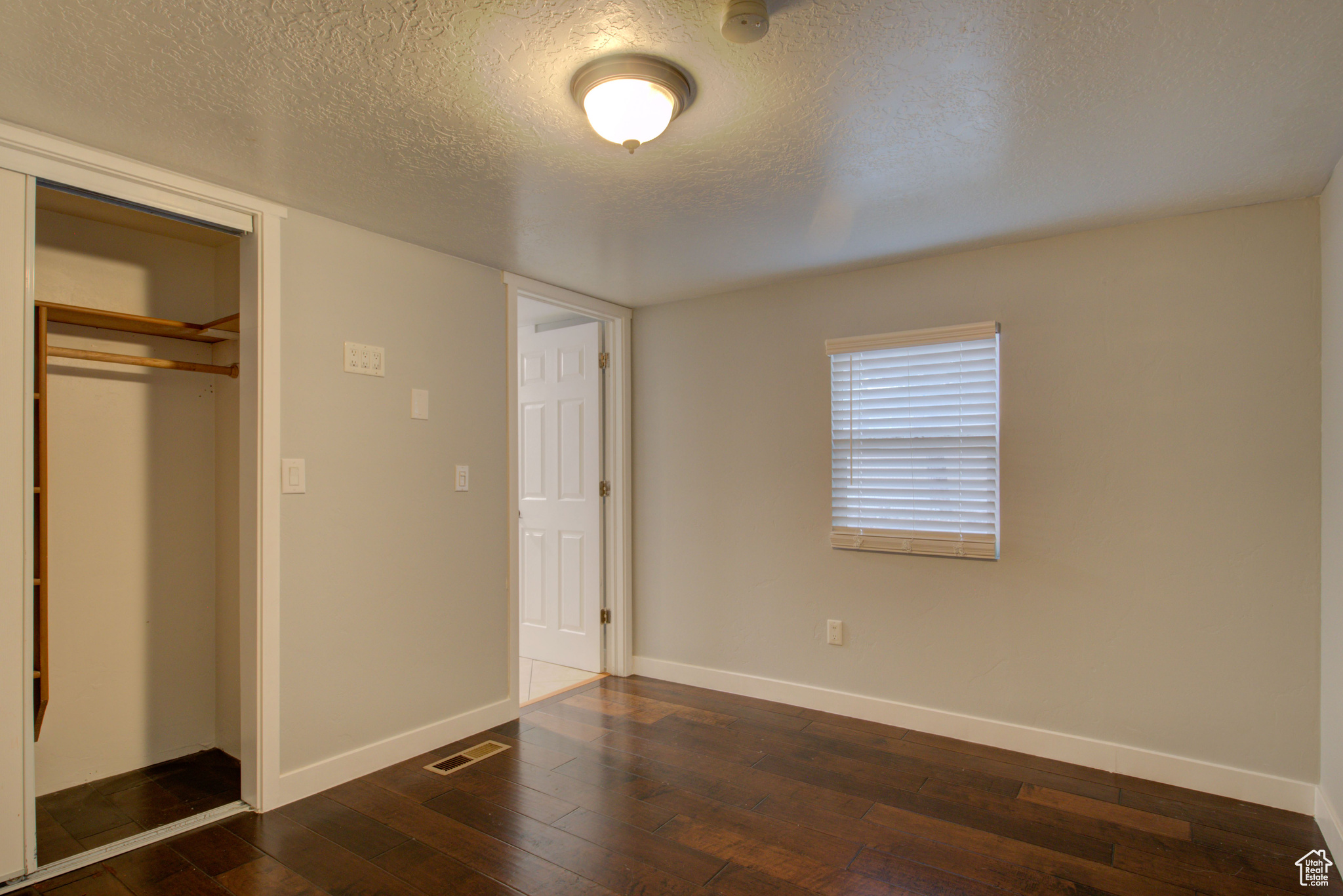 Unfurnished bedroom with dark hardwood / wood-style flooring, a textured ceiling, and a closet