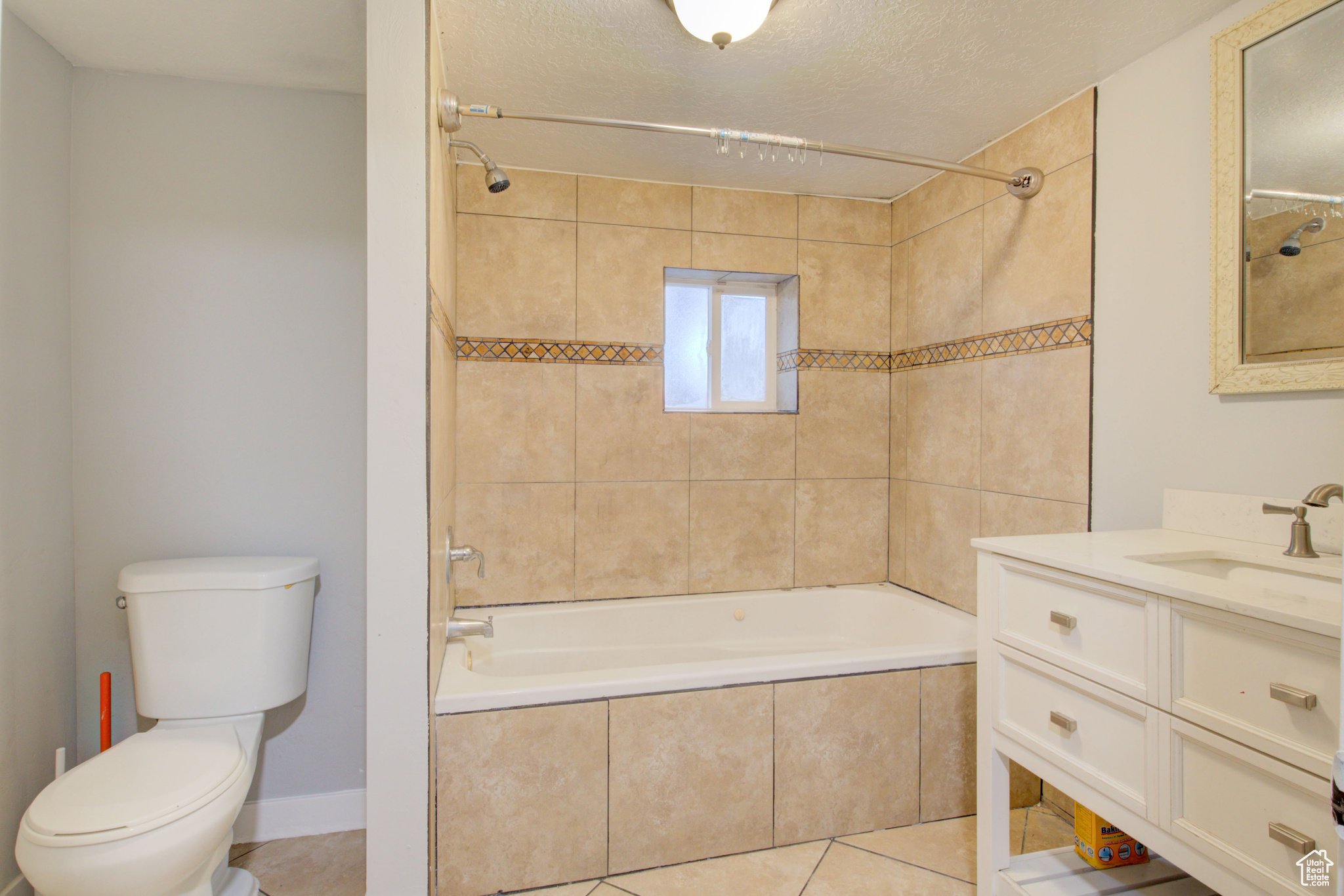 Full bathroom with tiled shower / bath combo, tile patterned floors, a textured ceiling, toilet, and vanity