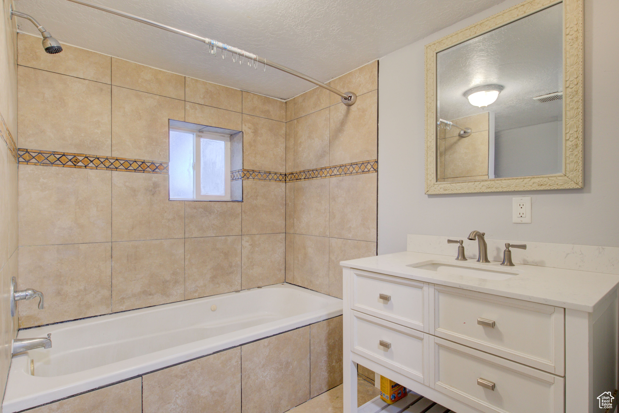 Bathroom with vanity, a textured ceiling, and tiled shower / bath