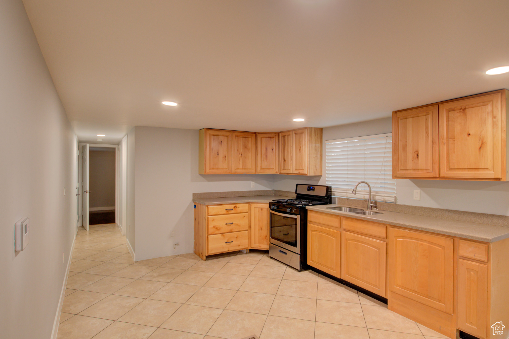 Kitchen featuring light tile patterned flooring, sink, light brown cabinetry, and stainless steel range with gas stovetop