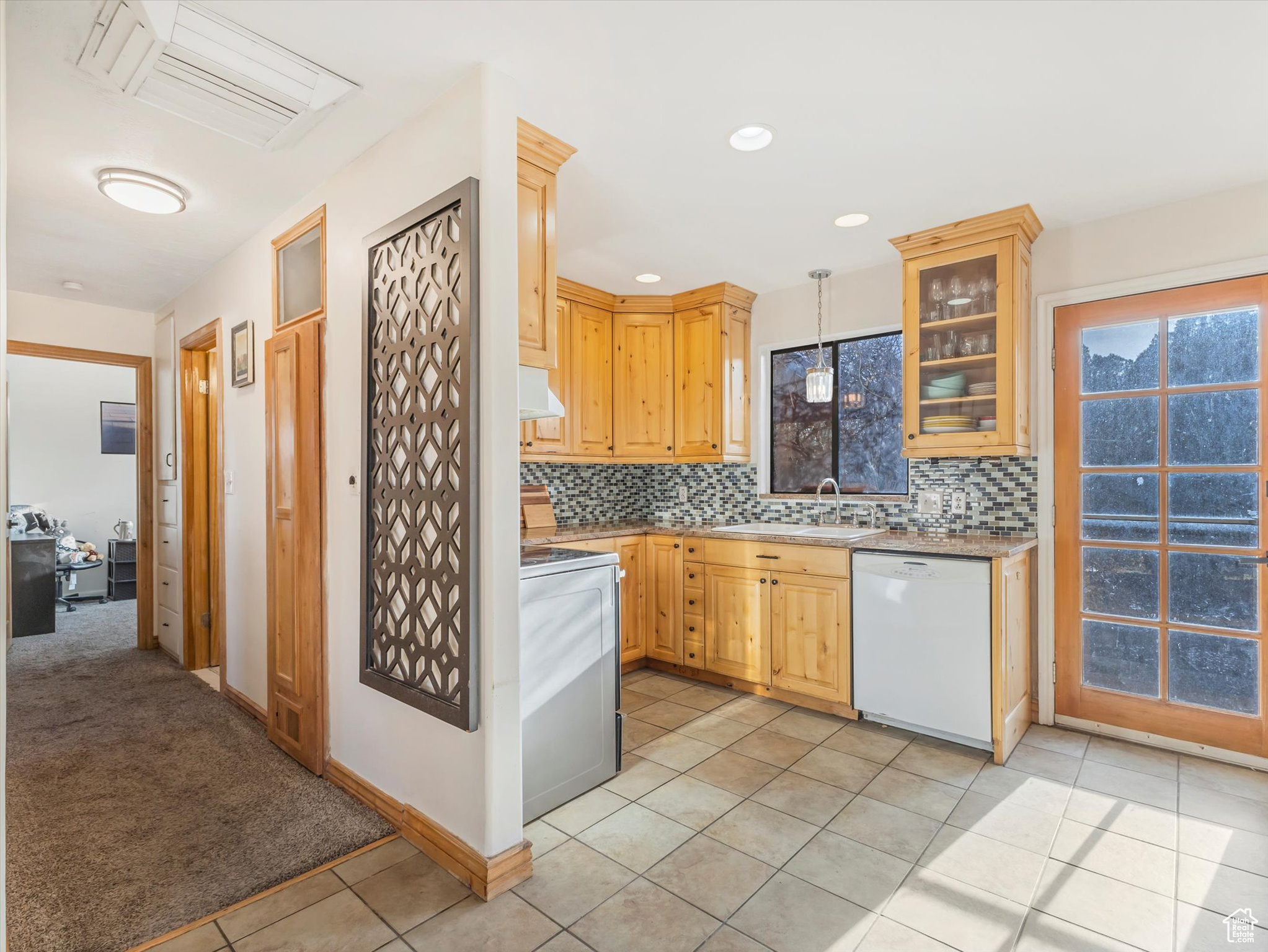 Kitchen featuring backsplash, white dishwasher, hanging light fixtures, range hood, and range