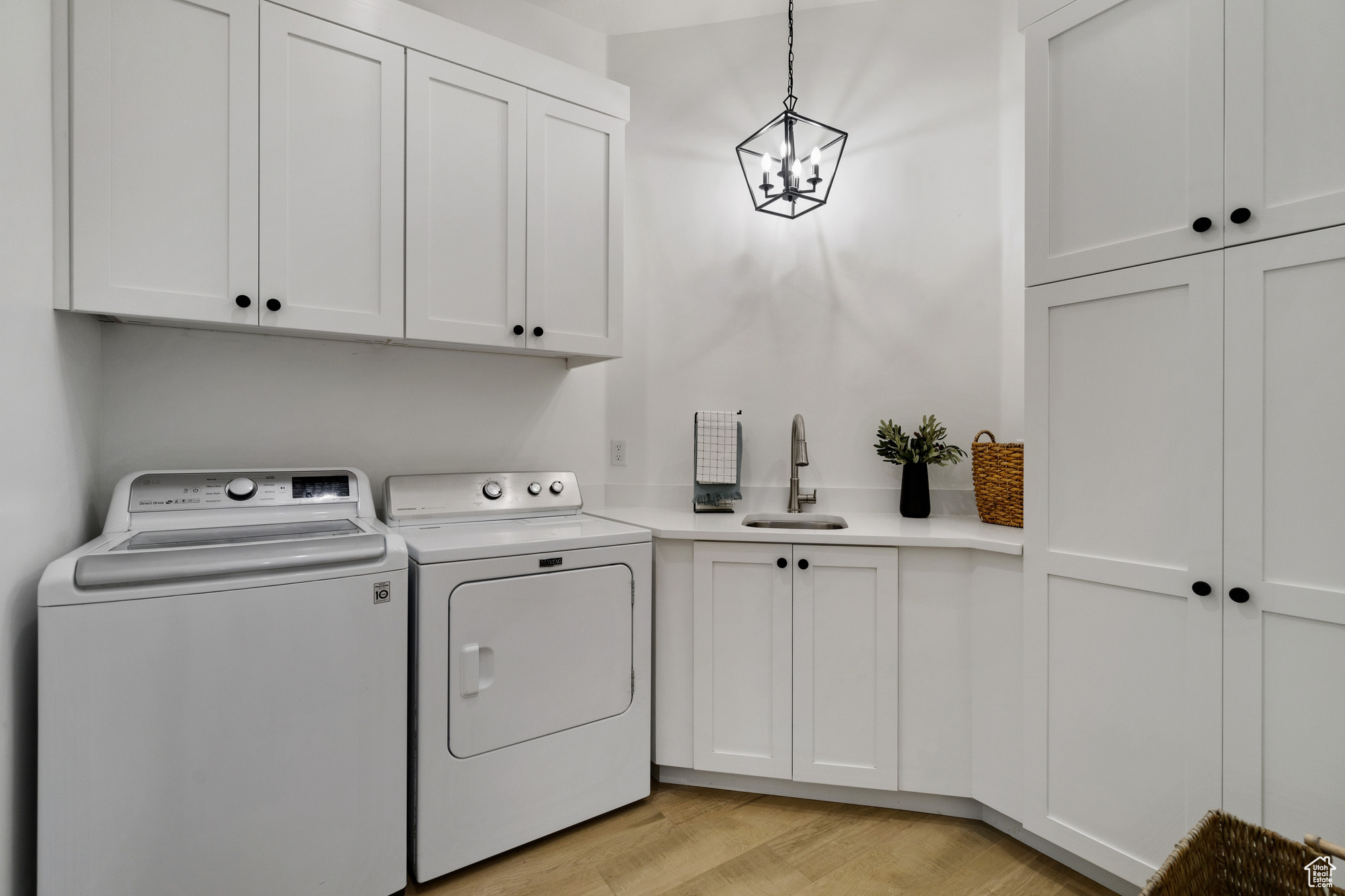 Laundry area with washer and clothes dryer, cabinets, an inviting chandelier, sink, and light hardwood / wood-style floors