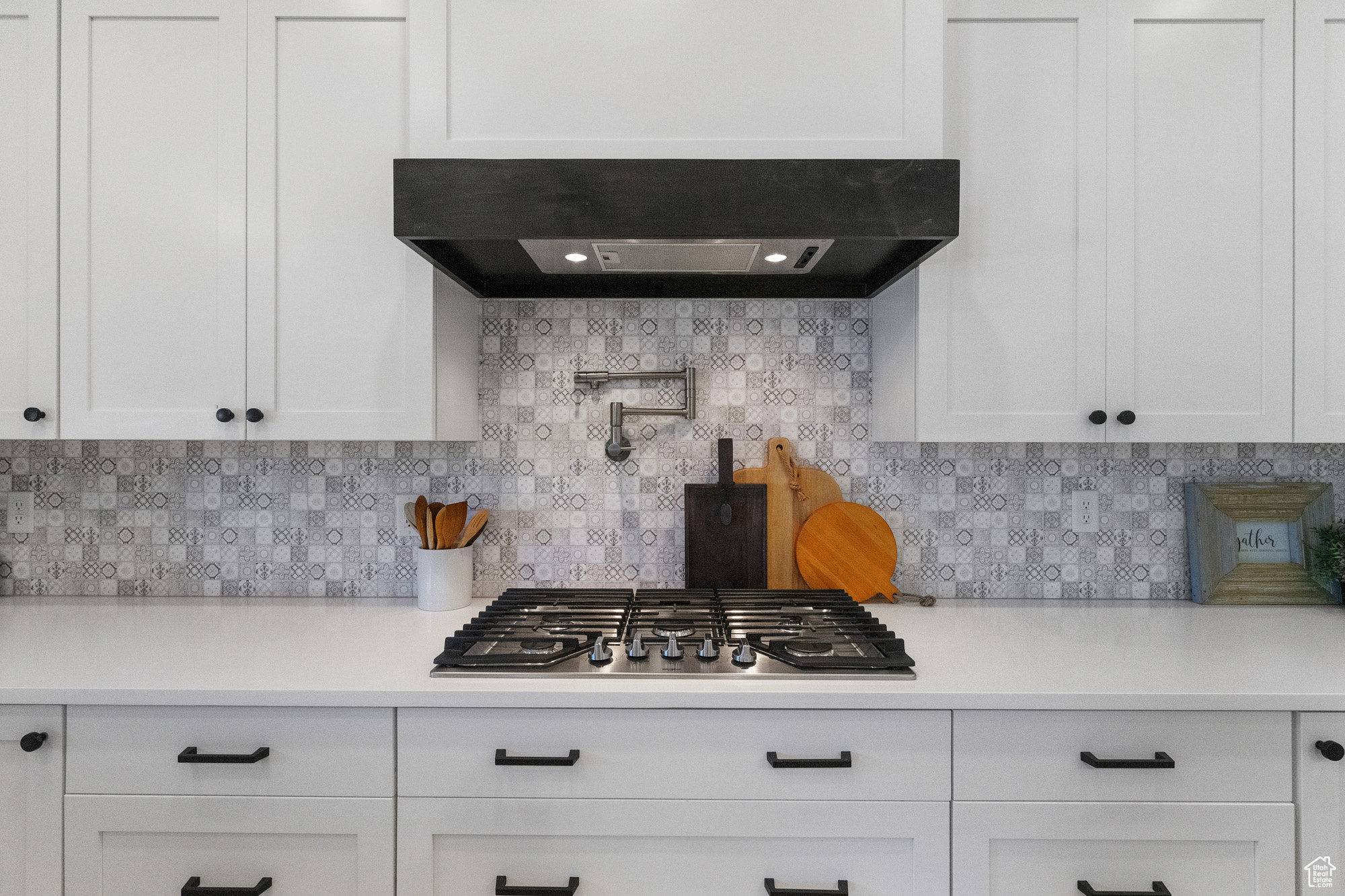 Kitchen featuring exhaust hood, white cabinetry, backsplash, and stainless steel gas cooktop