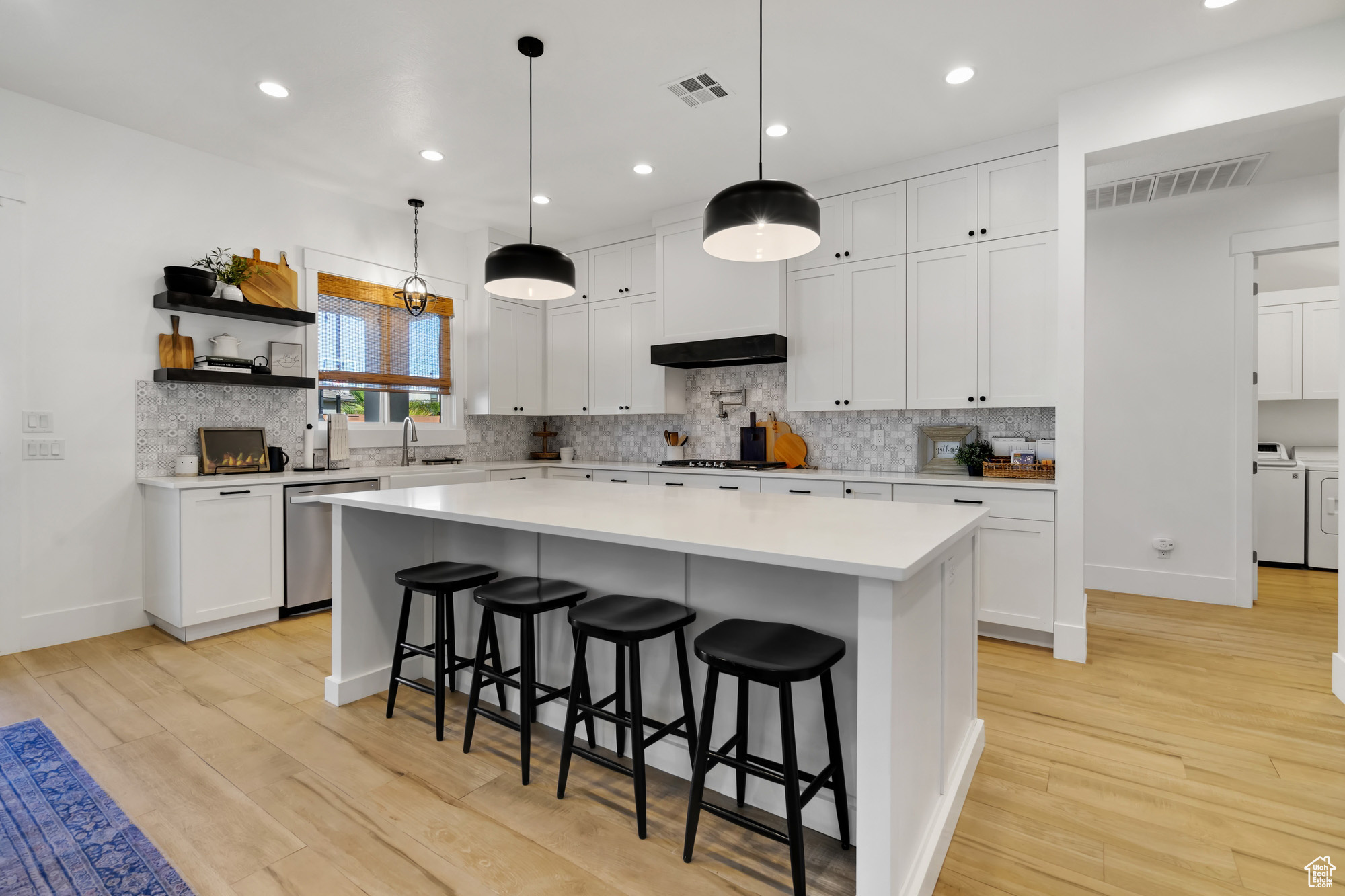 Kitchen featuring dishwasher, hanging light fixtures, washing machine and dryer, a kitchen island, and white cabinetry