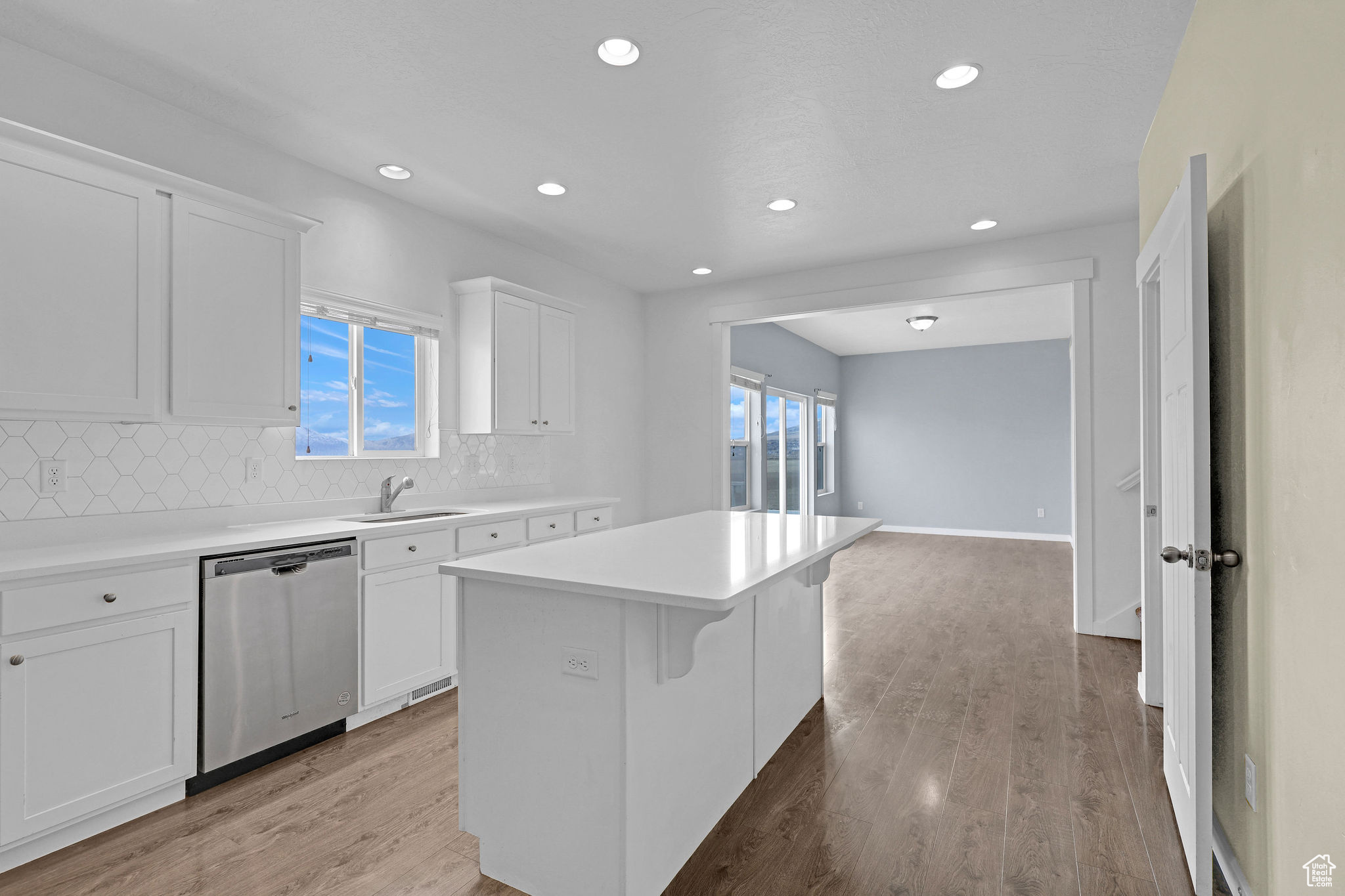 Kitchen with decorative backsplash, light wood-type flooring, stainless steel dishwasher, a kitchen island, and white cabinetry