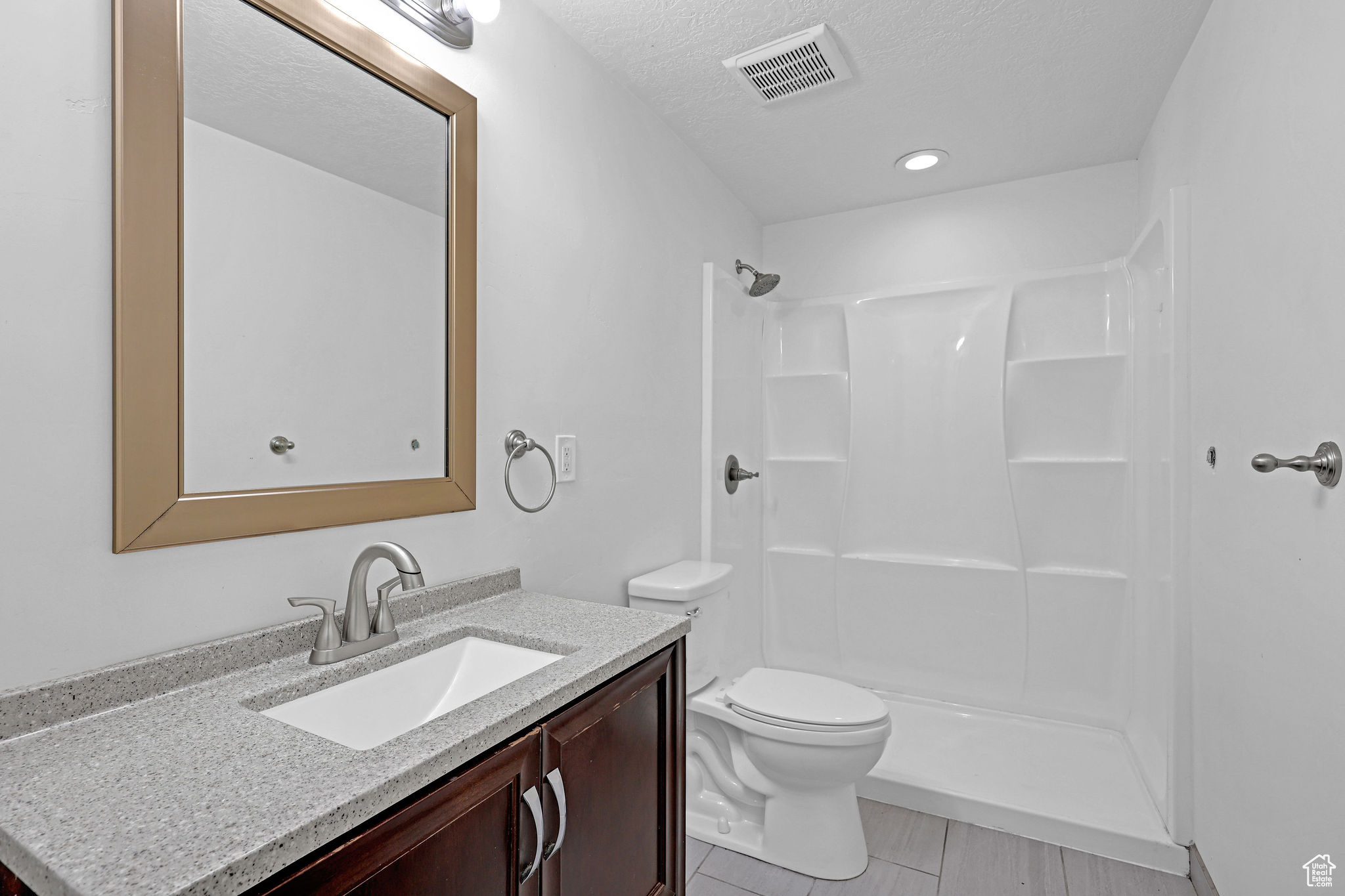 Bathroom featuring walk in shower, vanity, a textured ceiling, and toilet