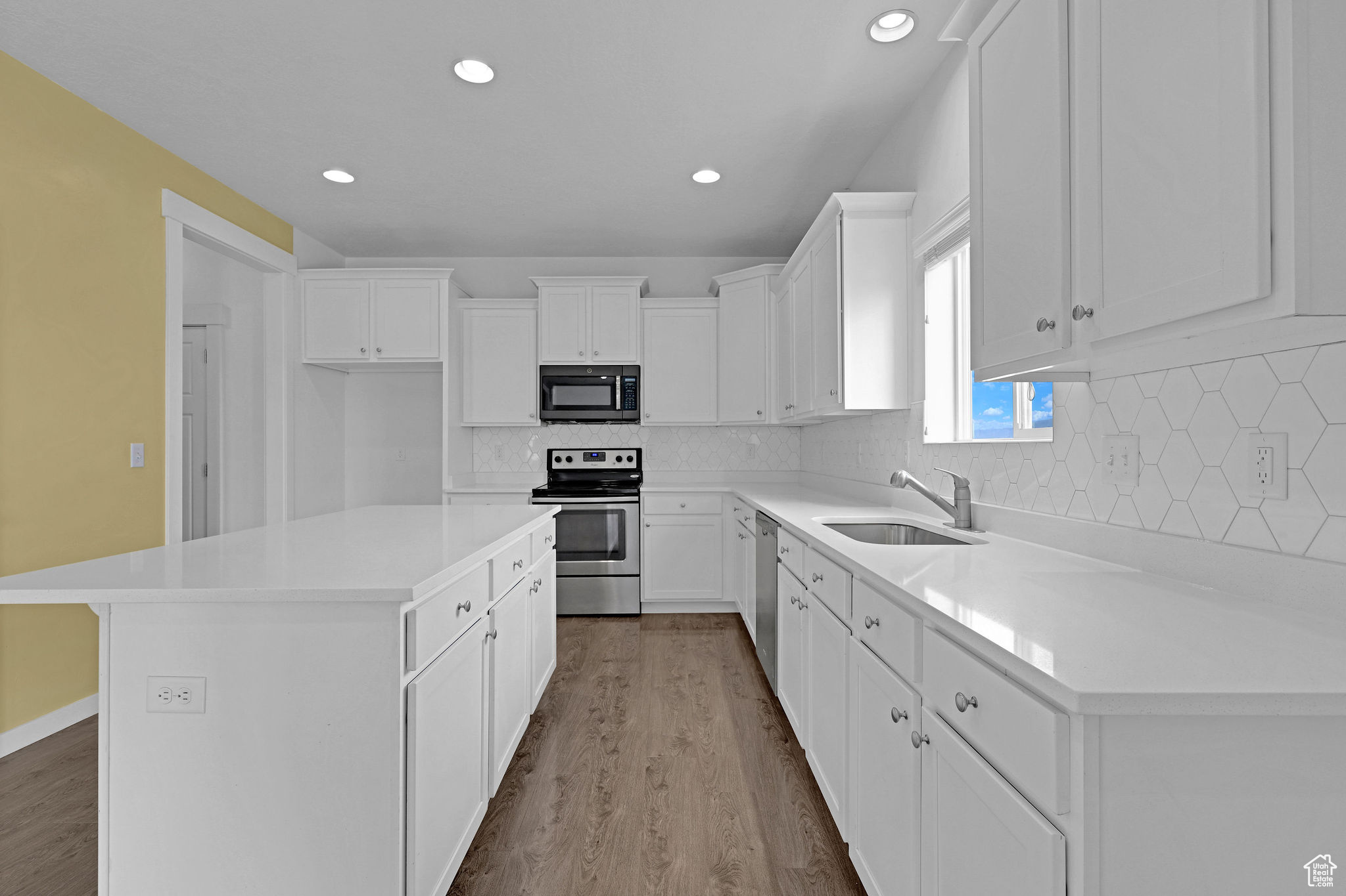 Kitchen with sink, stainless steel appliances, a kitchen island, light hardwood / wood-style flooring, and white cabinets