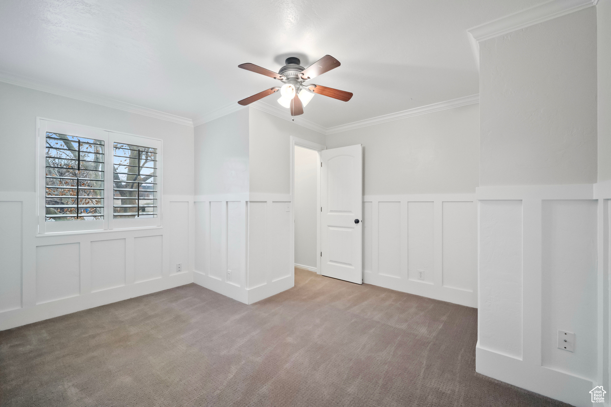 Carpeted empty room featuring ceiling fan and ornamental molding