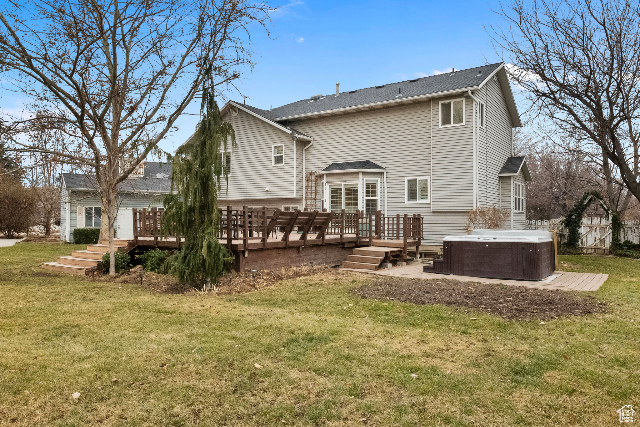 Back of property with a hot tub, a deck, central AC unit, and a lawn