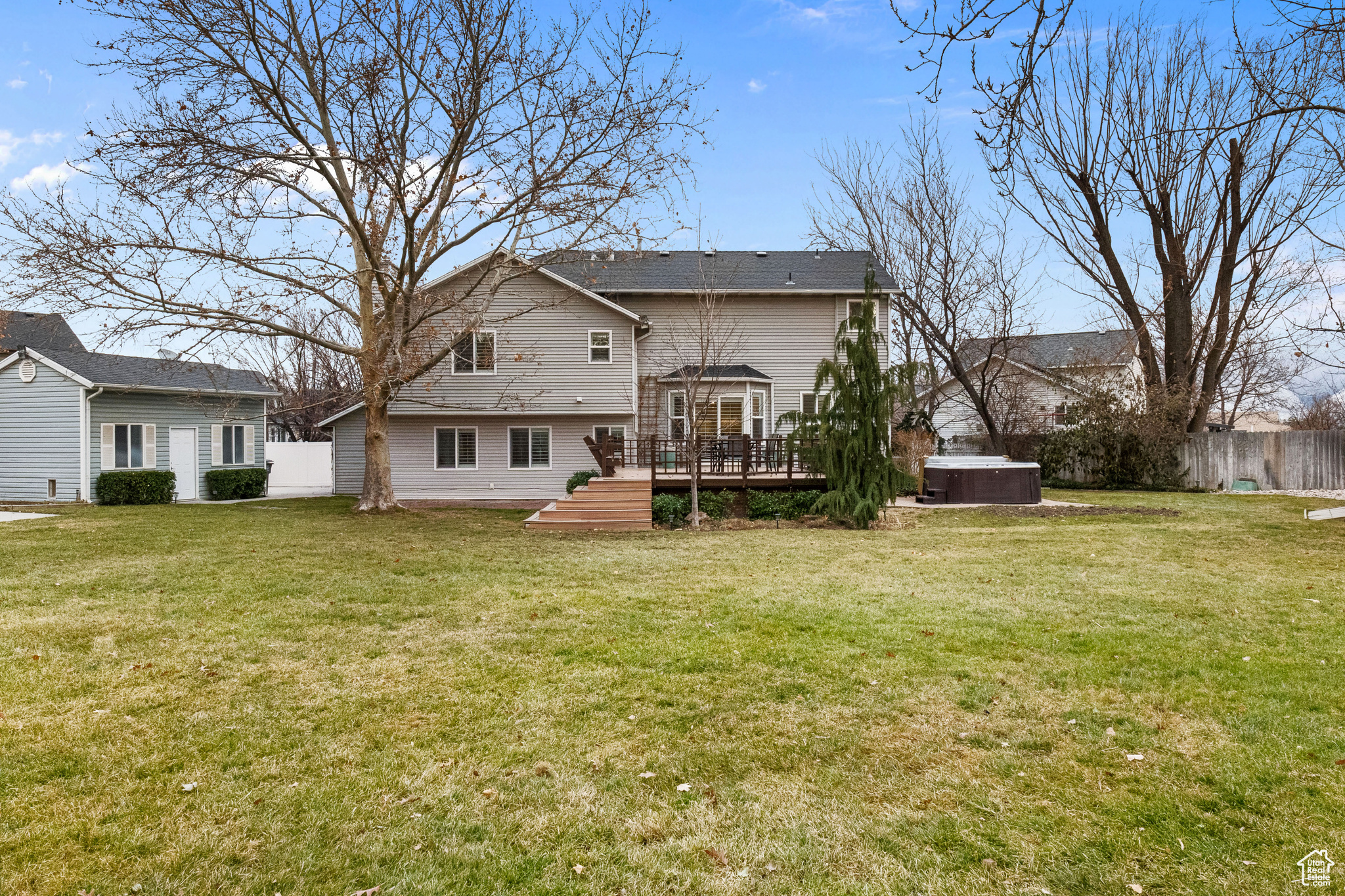 Rear view of house with a lawn, a wooden deck, and a hot tub