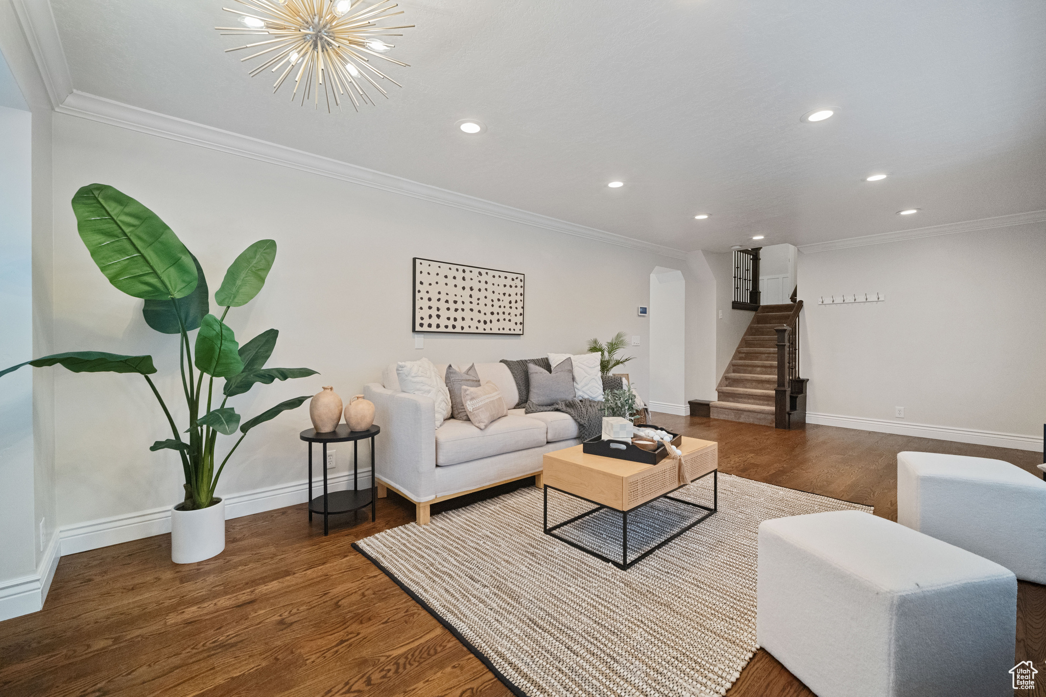 Living room with dark hardwood / wood-style flooring, crown molding, and a chandelier