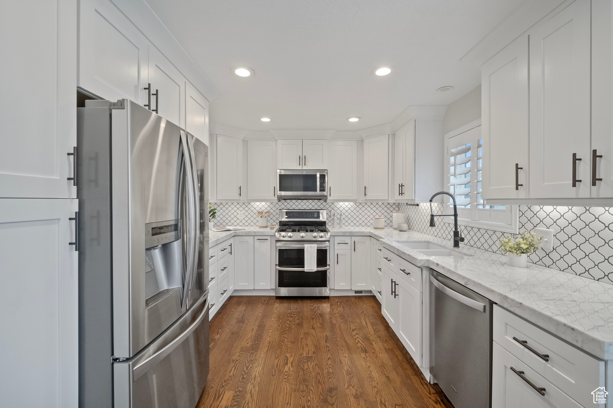 Kitchen featuring light stone countertops, appliances with stainless steel finishes, dark wood-type flooring, sink, and white cabinetry