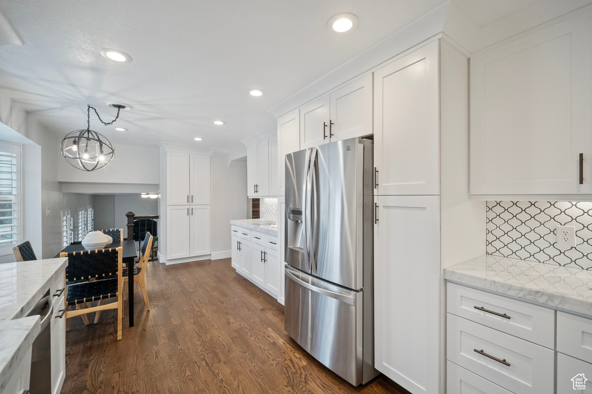 Kitchen with dark wood-type flooring, stainless steel appliances, pendant lighting, decorative backsplash, and white cabinets