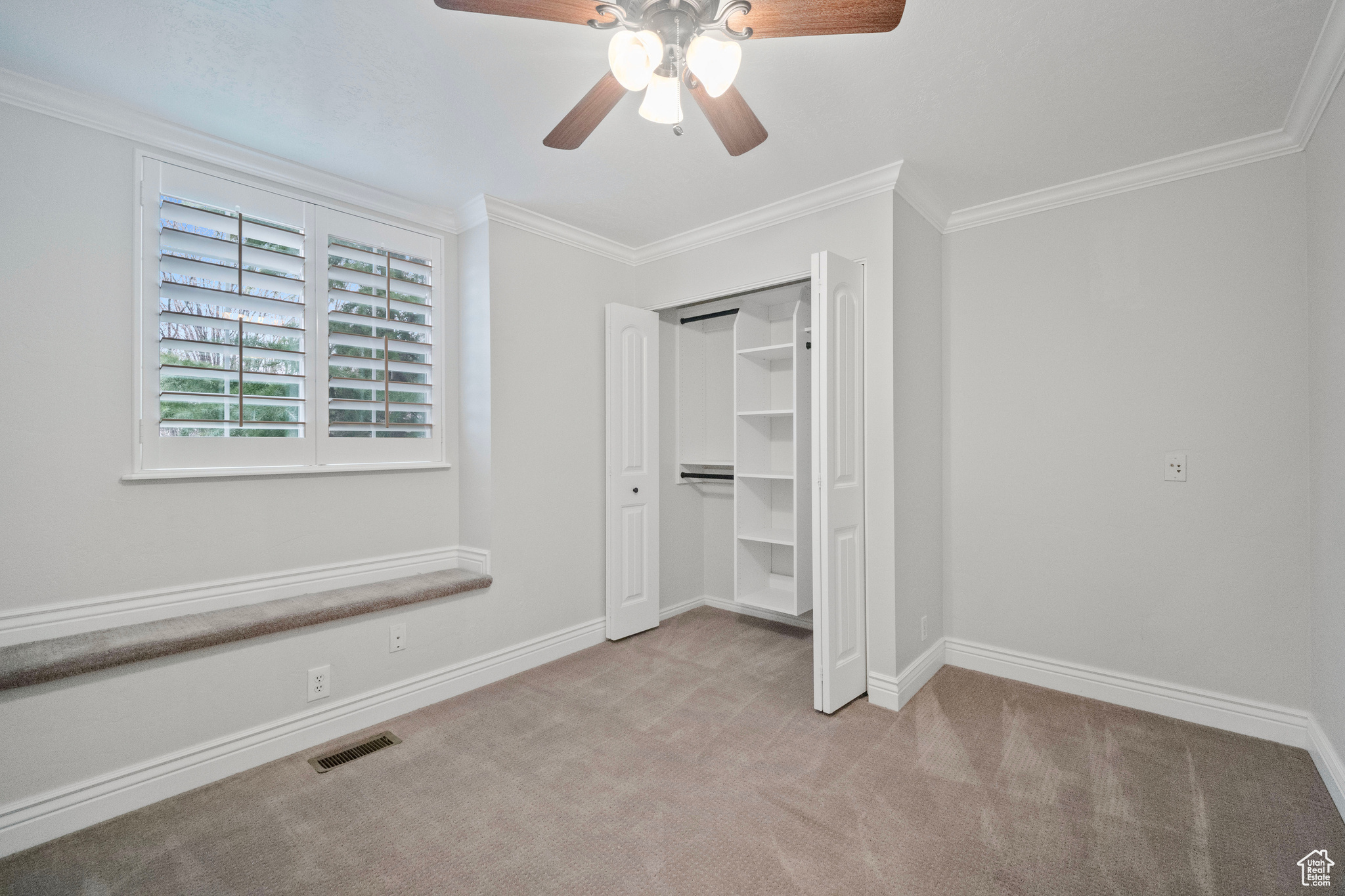 Unfurnished bedroom with light carpet, a closet, ceiling fan, and crown molding