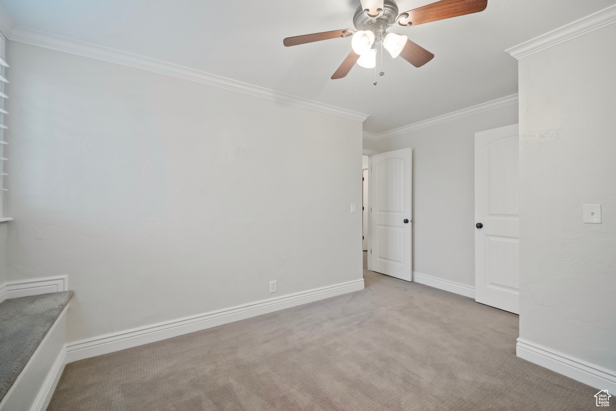 Empty room featuring ceiling fan, light colored carpet, and ornamental molding